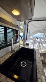 Inside this RV rental: modern sink, comfortable unmade bed, and a scenic mountain view from the pop-out area.
