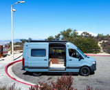 This blue camper van rv rental, with its side door open revealing a modern interior kitchen, is parked at a scenic lookout.