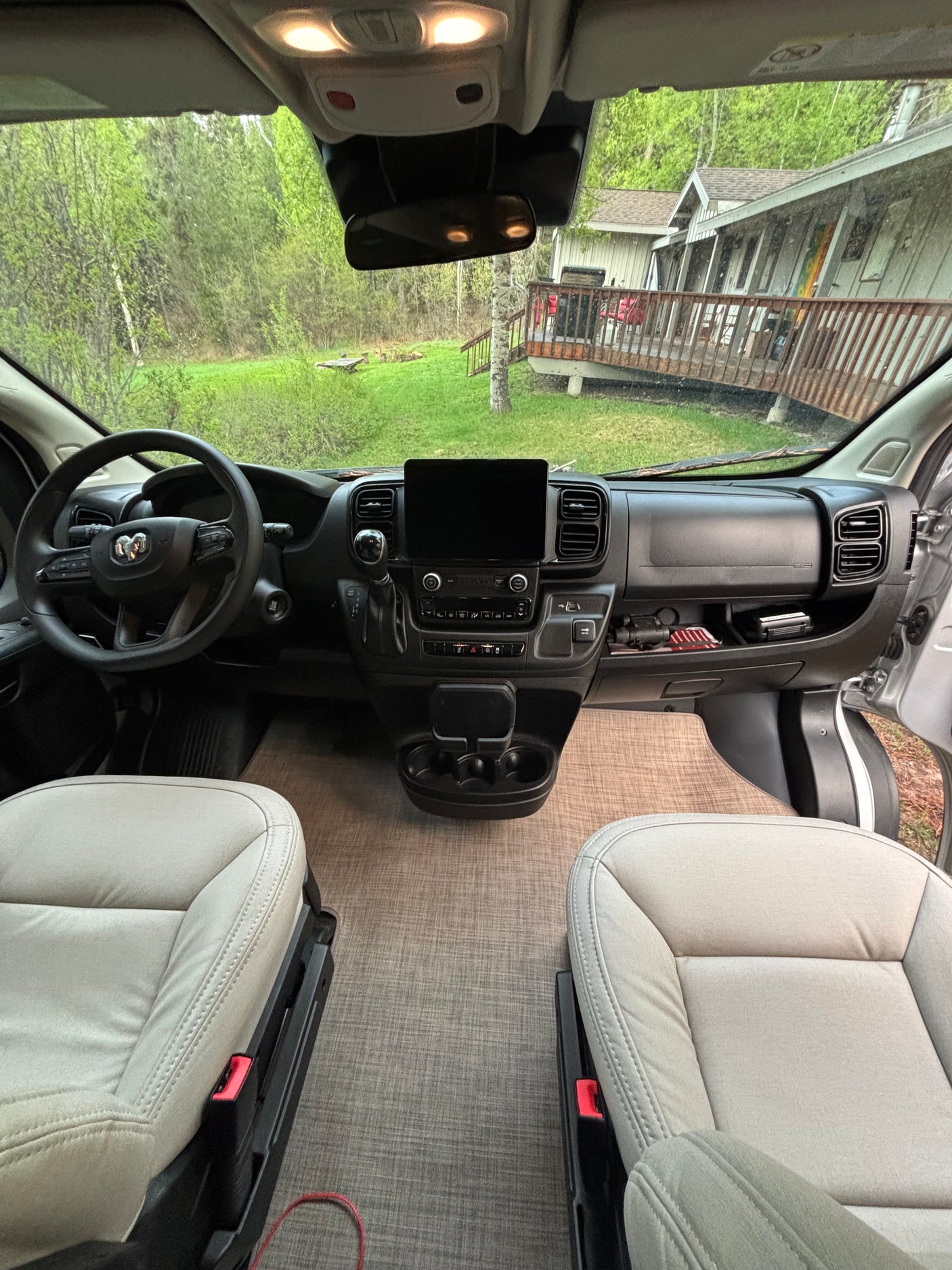 Inside this RV rental: front cabin with comfortable seats, a modern dashboard, and a scenic forest view outside a home.
