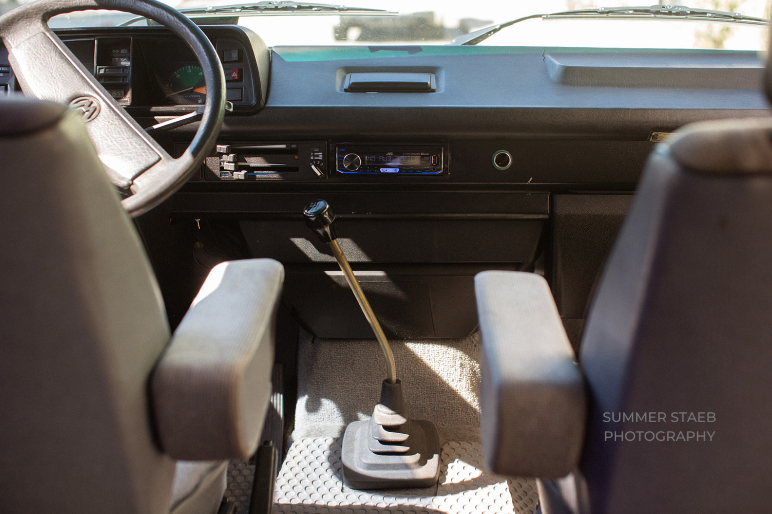 Interior of an RV rental: dashboard, steering wheel, and manual gear shift in a classic VW van.