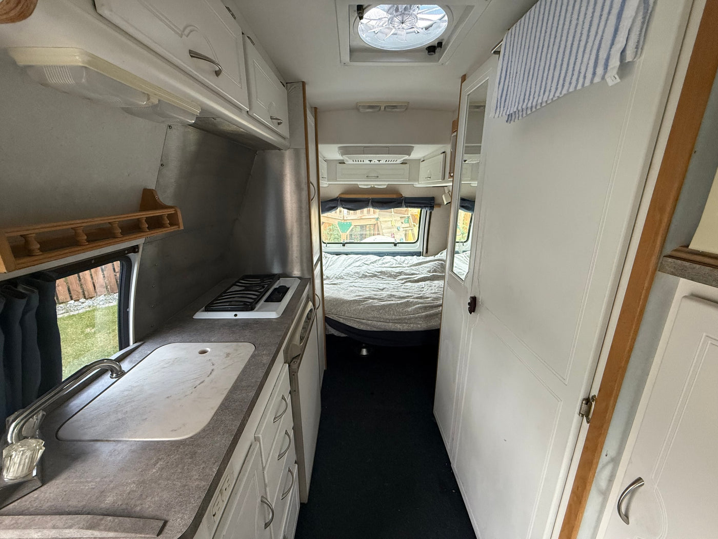 View inside an RV rental showing a compact kitchen with sink and stove, leading to a bed. Ideal for travel adventures. — photo 4