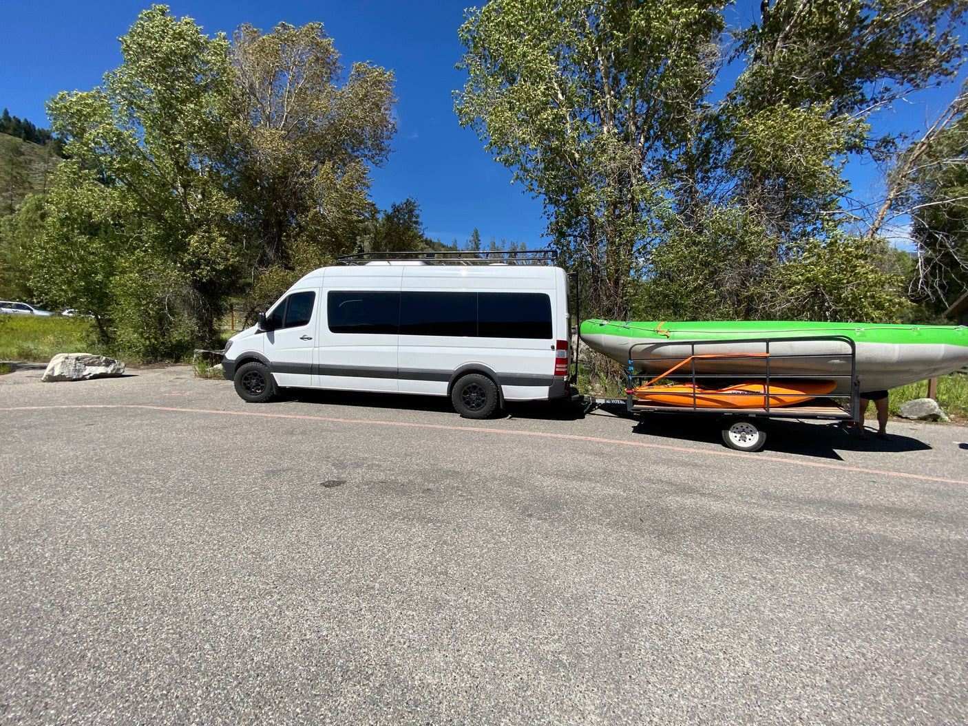 RV rental Sprinter van with roof rack towing a trailer carrying a raft and kayak, ready for outdoor adventure.