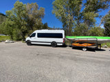 RV rental Sprinter van with roof rack towing a trailer carrying a raft and kayak, ready for outdoor adventure.