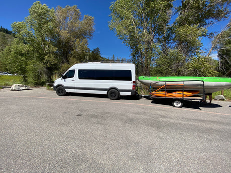 RV rental Sprinter van with roof rack towing a trailer carrying a raft and kayak, ready for outdoor adventure.