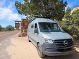 Grey rv rental van at Zion National Park entrance, with the park sign, road, and cliffs in view.