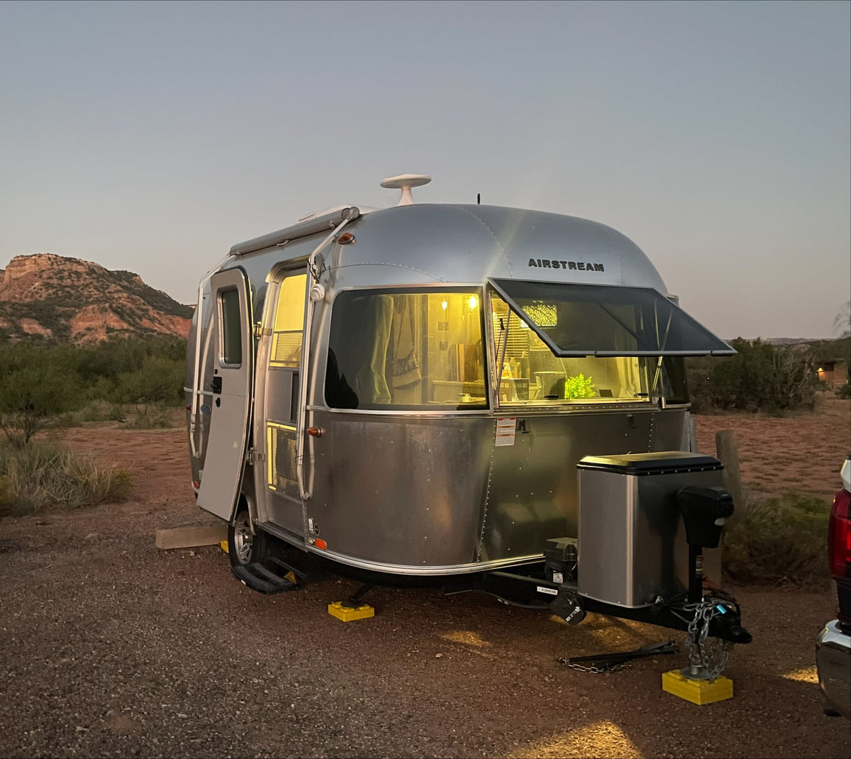 Experience an Airstream rv rental: a silver travel trailer glowing at dusk, parked in a scenic desert campground with mountains.