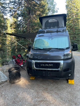 Ram ProMaster rv rental camper van with pop-top and awning, leveled at a serene forest campsite. Outdoor comfort!