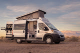 Silver pop-top RV rental in a desert landscape with mountains. Open doors reveal the camper van's inviting interior.