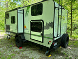 This sleek NO BO travel trailer, featuring an expandable side and off-road tires, is an ideal RV rental for exploring wooded campsites.
