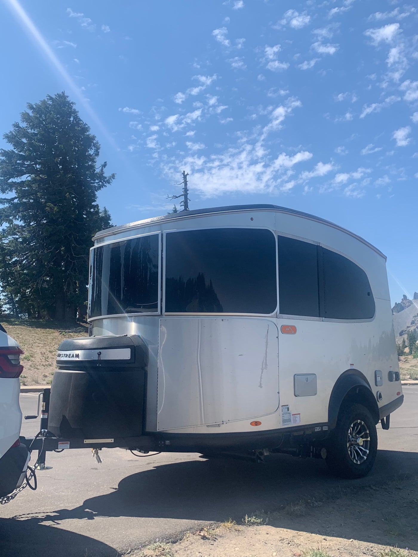  parked on asphalt with forested hills and clear skies behind it.|Sleek silver travel trailer — photo 6