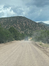 A dark SUV drives on a dusty dirt road through green mountains under cloudy skies. Perfect for an rv rental adventure!