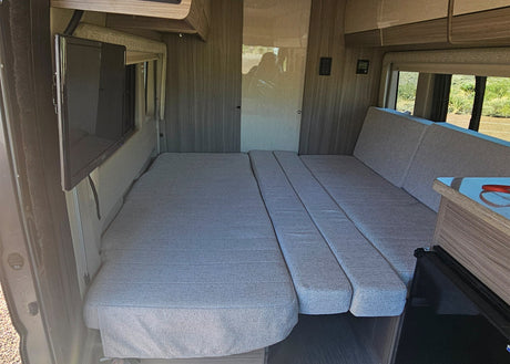 Inside an RV rental: a flexible grey cushion bed/seating area, TV, and scenic rear windows provide comfort on the road.