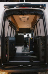 View inside an RV rental: a custom camper van interior with modular storage, seating, and an overhead AC unit from the rear doors.