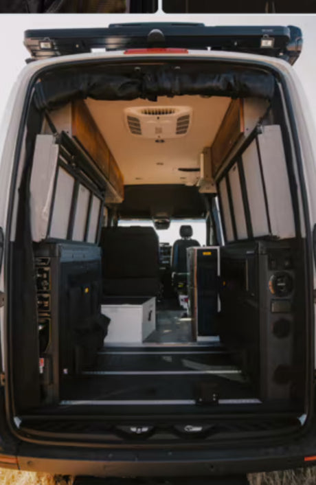 View inside an RV rental: a custom camper van interior with modular storage, seating, and an overhead AC unit from the rear doors.