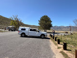 A white pickup truck with RV camper shell, an ideal RV rental for exploring scenic mountain roads. A man takes photos of snowy peaks.