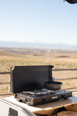 RV rental setup: Primus camping stove on a pull-out kitchen, ready for outdoor cooking in a scenic landscape.