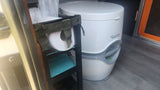 RV rental: White Porta Potti portable toilet beside a compact shelving unit with toilet paper.