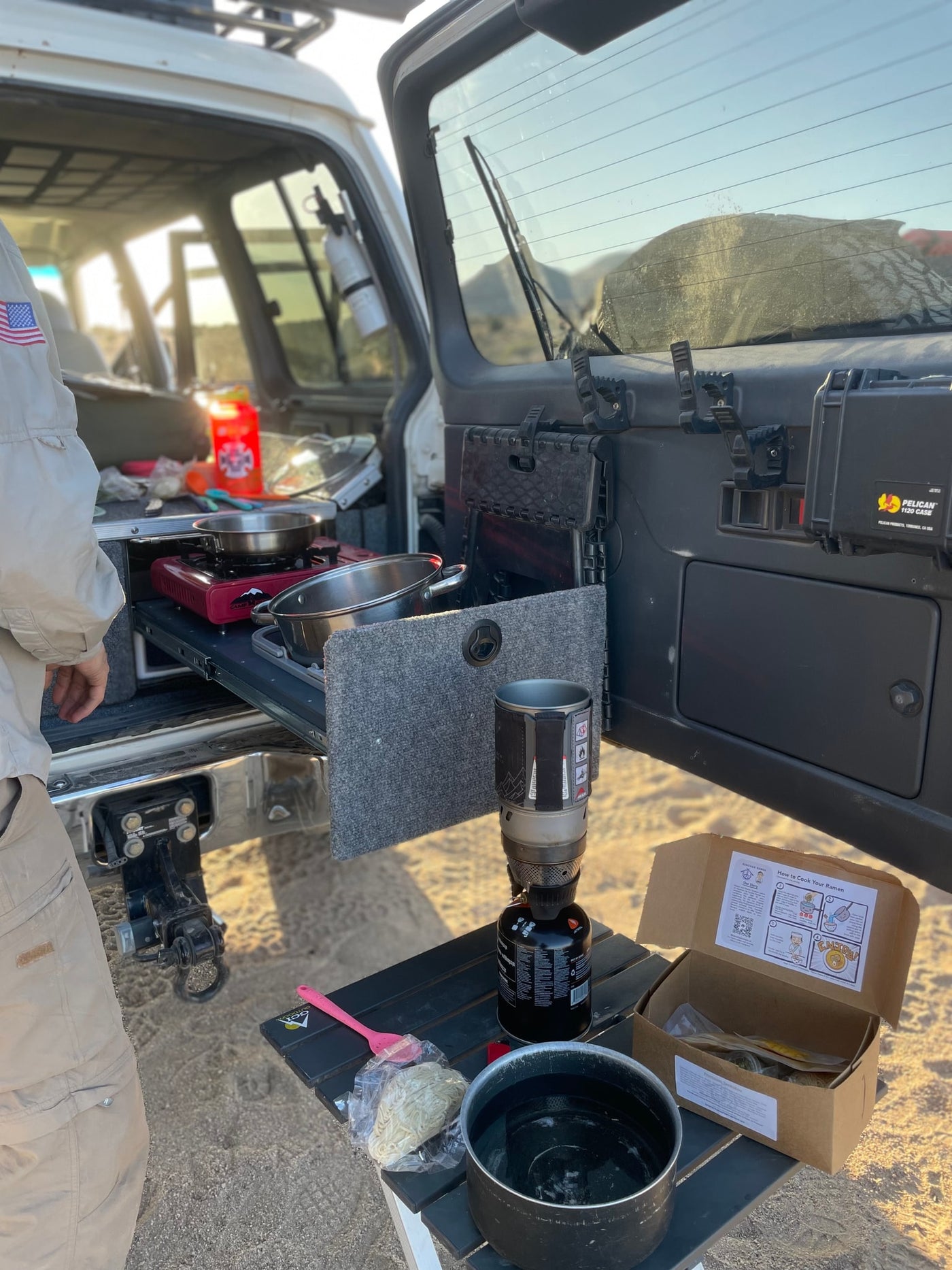 An RV rental's overland camp kitchen setup: cooking ramen with portable stoves and vehicle-mounted gear for an outdoor meal. — photo 13