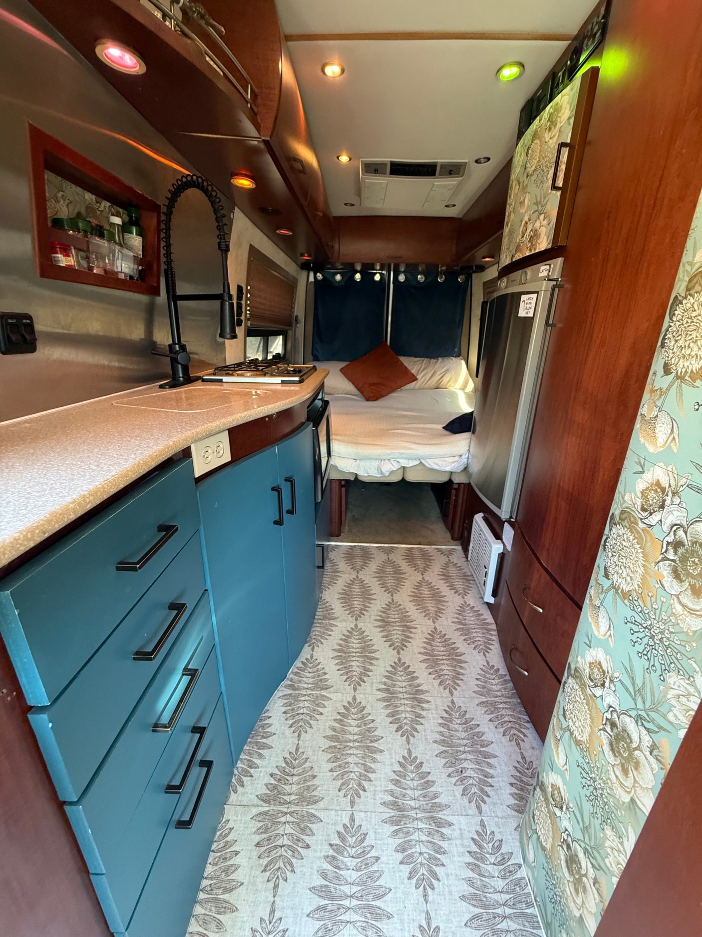 Explore this stylish rv rental: a cozy interior featuring a compact kitchen, bed, fridge, and unique lighting.