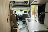 View inside a modern RV rental. This camper van features a well-equipped kitchen, comfortable seating, and a clear view to the front.