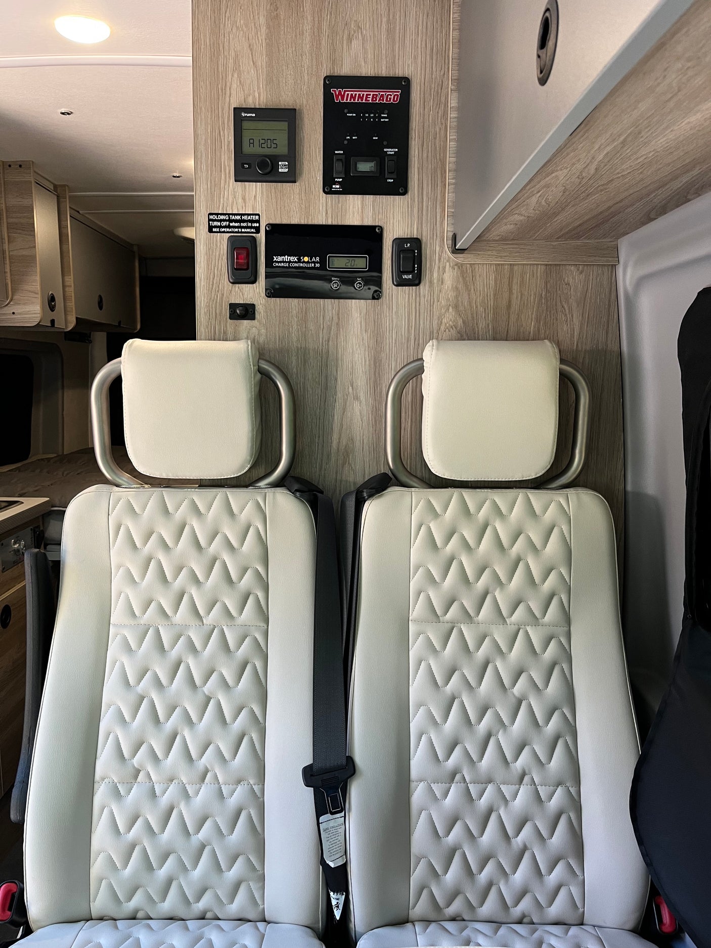 Inside an RV rental: dual passenger seats with textured upholstery and wall-mounted control panels for Truma and solar.