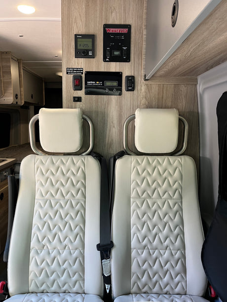 Inside an RV rental: dual passenger seats with textured upholstery and wall-mounted control panels for Truma and solar.