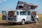 Explore van life with this RV rental: a white camper van with an open rooftop tent, ladder, and rear kitchen setup.