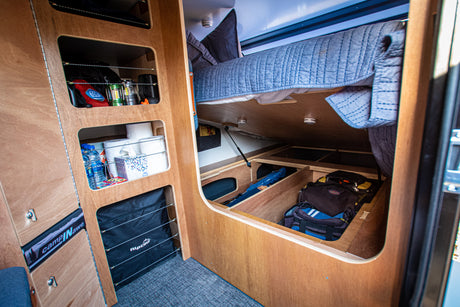 RV rental interior: organized wooden shelves with supplies, a cozy bunk bed, and ample under-bed storage.