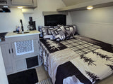  is set up at a scenic lakeside campsite with an open awning and fire pit.|RV rental at a serene lakeside campsite