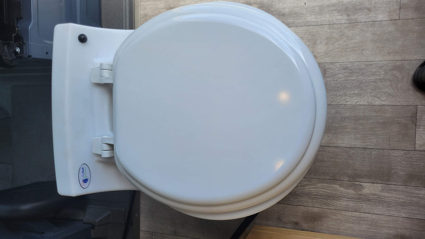 This white dry flush toilet with its lid closed is perfect for any RV rental adventure. A top-down view shows the unit and wood-look floor.