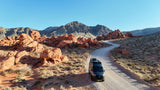 RV rental van on a desert road, surrounded by stunning red rock formations & mountains under a clear sky. Ideal for adventure travel.