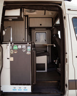 Step into this RV rental camper van, featuring a modern kitchenette, dining area, and travel stickers on the fridge door.