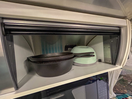 RV rental kitchen: compact cabinet with tambour door, storing cast iron pans and a green bowl above the microwave.