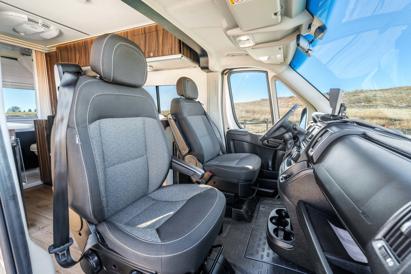 Experience this RV rental's inviting front cabin. Swivel seats, dashboard & view into the comfortable camper interior.