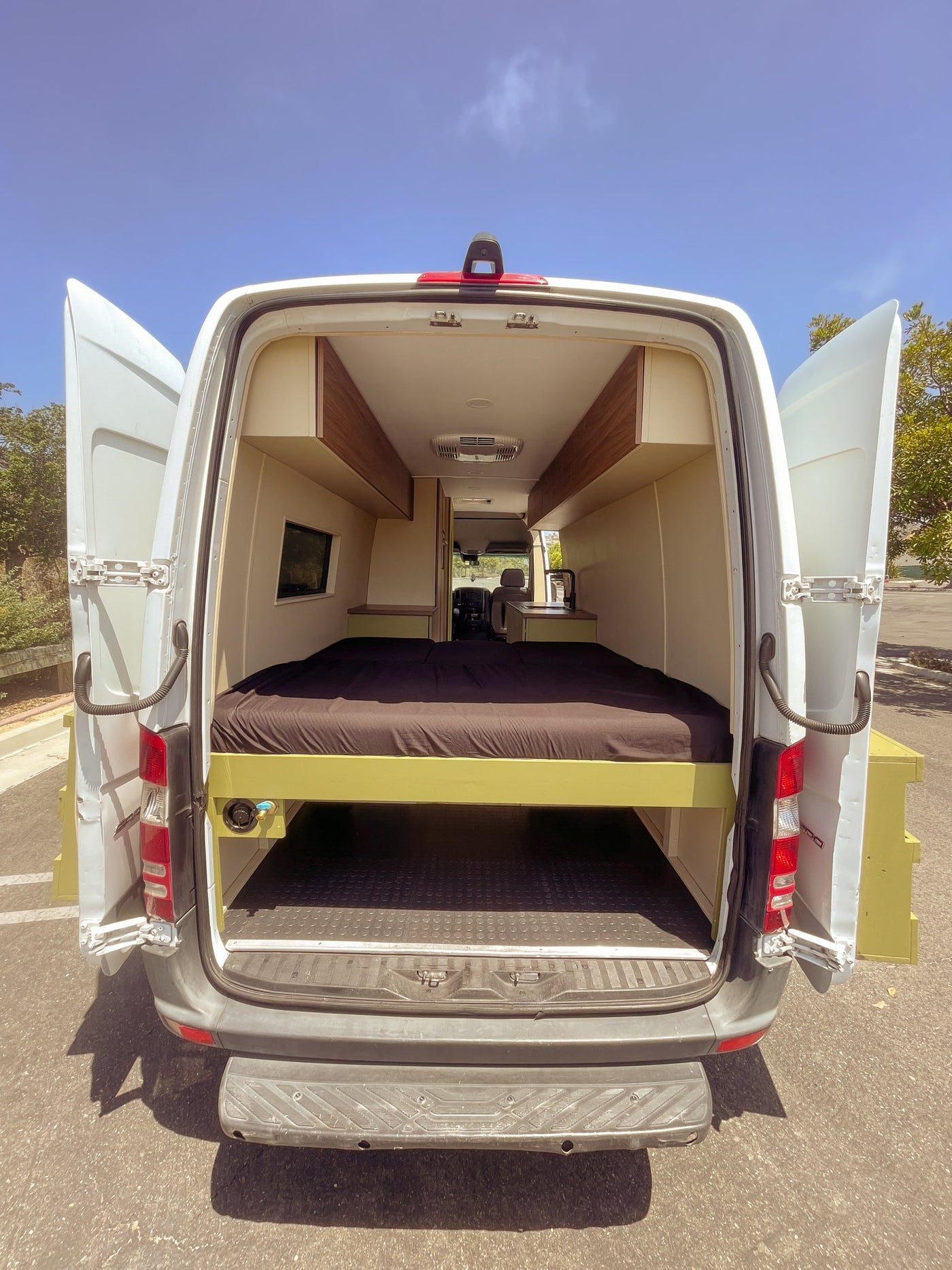 Interior of an RV rental campervan with open doors: a bed, under-bed storage, overhead compartments, and a kitchen. — photo 10