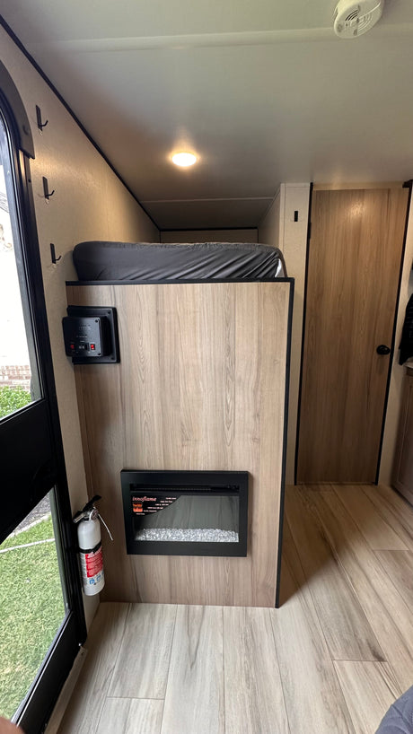 RV rental's cozy interior: bunk bed, electric fireplace, control panel, and fire extinguisher for safety.