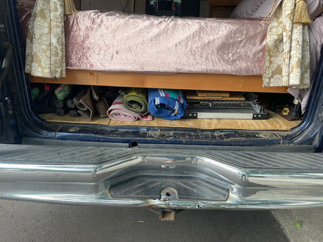 RV rental van interior: Organized under-bed storage for camping essentials like a grill and mats, seen from the rear.