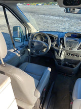 Inside an RV rental, view from rear to front showing the driver's seat, steering wheel, and dashboard of a Ford van.
