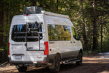 White Thor Tranquility Sprinter RV rental van with a bike rack, parked in a serene forest. Ideal for outdoor travel.