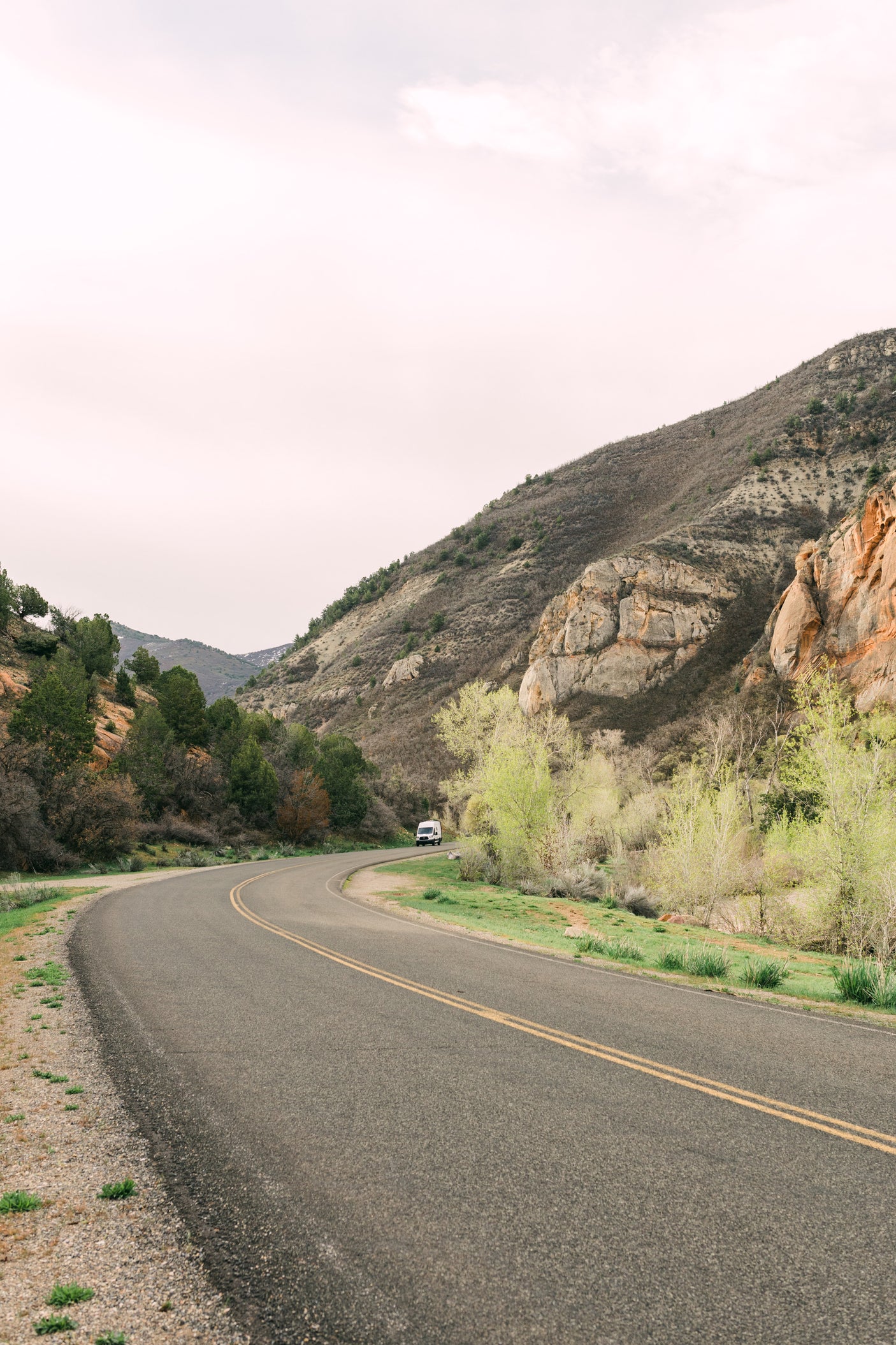Your RV rental adventure awaits! A white van on a winding road through mountains and new spring foliage.