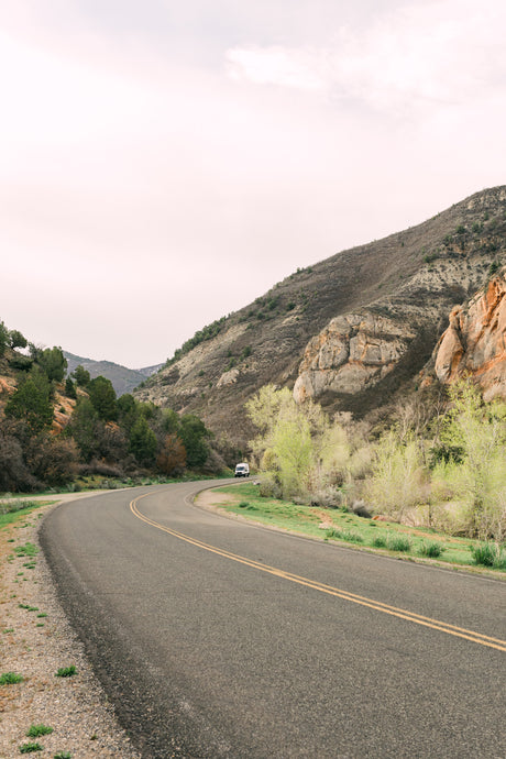 Your RV rental adventure awaits! A white van on a winding road through mountains and new spring foliage.