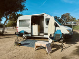 Campsite bliss with an rv rental! White camper van, surfboard, chairs, and grill ready for adventure under blue skies.