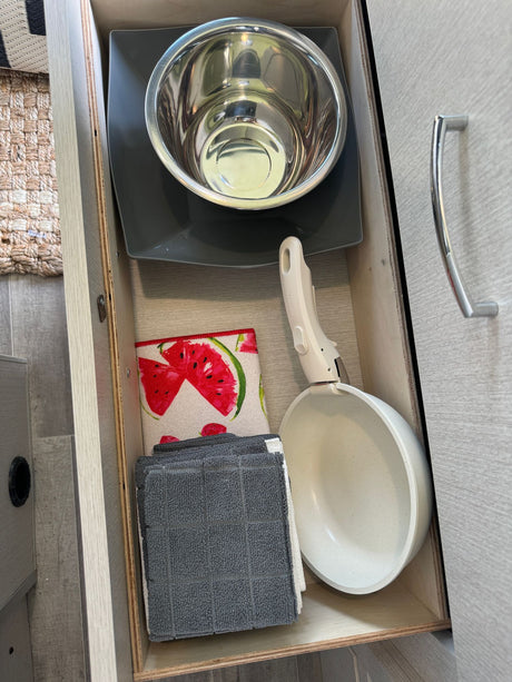RV rental kitchen drawer: a mixing bowl, plate, pan with a detachable handle, and kitchen towels, neatly stored.