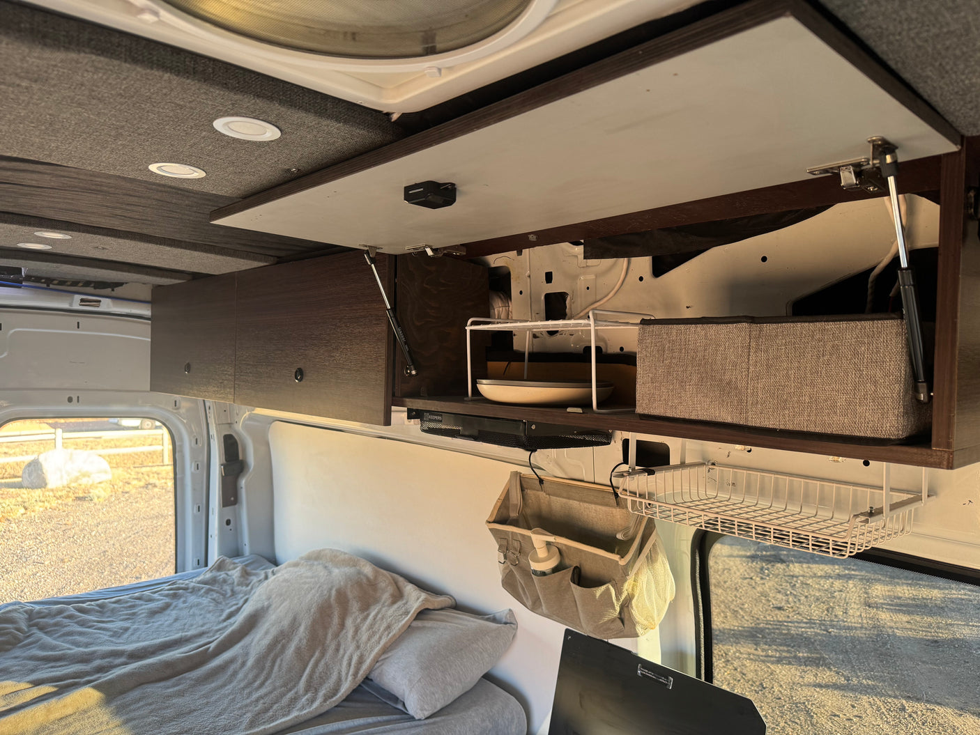 RV rental interior: Overhead storage with organizers, a compact dish shelf, and a comfortable bed for road trips.