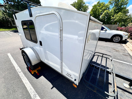 White 5x8 Hiker compact travel trailer, an ideal RV rental with roof and rear cargo racks for adventures.