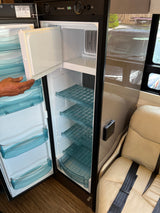Empty Dometic RV refrigerator, revealing shelves and door bins. A hand holds the top door. Great for your next rv rental adventure!