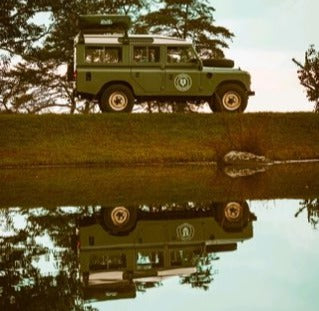 An iconic green Land Rover, ideal for an RV rental adventure, perfectly mirrored in calm water, ready for exploration.