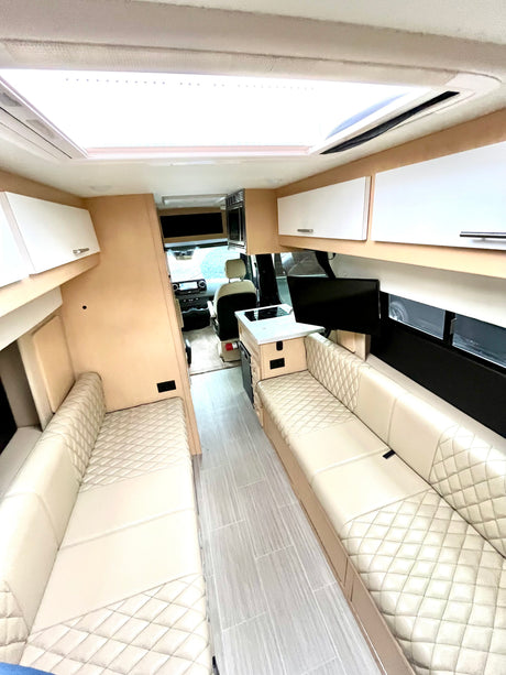 Spacious RV interior with light quilted leather seating, central aisle, and kitchen area looking towards the driver's cabin, perfect for an rv rental.