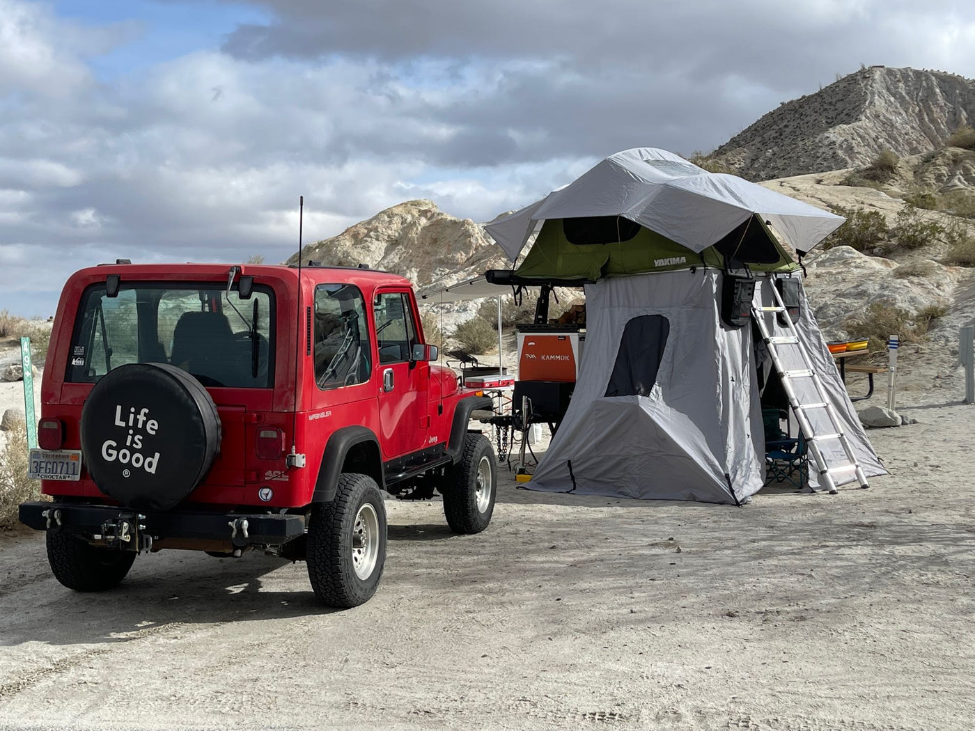  perfect for your next camping trip.|Interior view of a vibrant green RV rental roof tent with open mesh windows revealing bright trees & blue sky.|This compact RV rental camper trailer with a green Yakima rooftop tent and ladder is set up for outdoor camping adventures.|Red Jeep & rooftop tent system set up for desert camping — photo 6