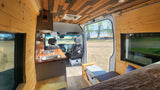 RV rental: Spacious wood-paneled camper van interior with kitchenette, bed, and scenic lake view.